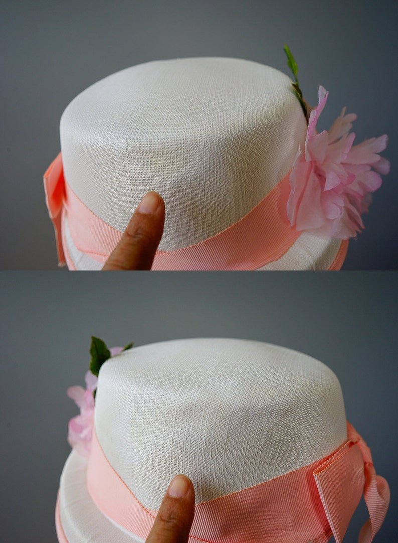 Op de afbeelding: Een witte strohoed met een roze lint en een roze bloemenversiering.