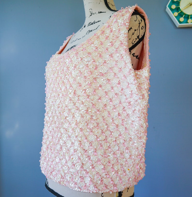 Pu&ograve; includere: Un top senza maniche di paillettes rosa e bianco. Il top &egrave; realizzato con piccole paillettes rotonde che sono cucite insieme in un motivo. Le paillettes sono di colore rosa chiaro con una lucentezza bianca.