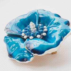 May include: A blue enamel flower brooch with a white center. The flower has a glossy finish and a slightly textured surface.