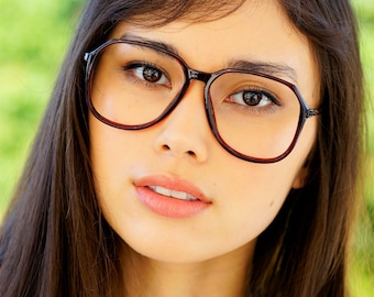 May include: A young woman with long dark brown hair wearing brown eyeglasses and a light pink blouse.
