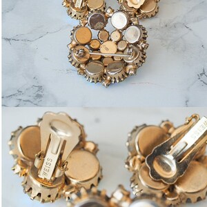 May include: A pair of gold tone clip-on earrings with a cluster of clear rhinestones. The earrings are marked "Weiss" on the back.
