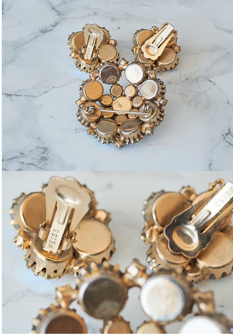 May include: A pair of gold tone clip-on earrings with a cluster of clear rhinestones. The earrings are marked "Weiss" on the back.