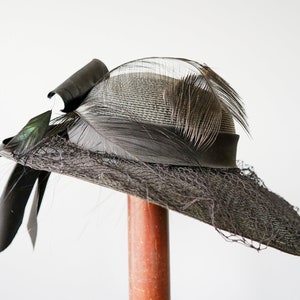 May include: A black and gray wide-brimmed hat with a black ribbon and feathers.