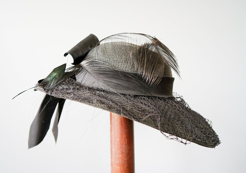 May include: A black and gray wide-brimmed hat with a black ribbon and feathers.