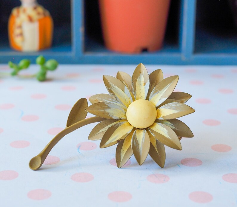 K&ouml;nnte beinhalten: Eine goldfarbene Metall-Sonnenblumenbrosche mit gelbem Zentrum. Die Sonnenblume hat eine strukturierte Oberfl&auml;che und ist mit wei&szlig;er Farbe akzentuiert.