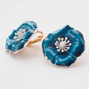 May include: A pair of blue enamel flower clip-on earrings with white centers. The earrings are gold-toned.