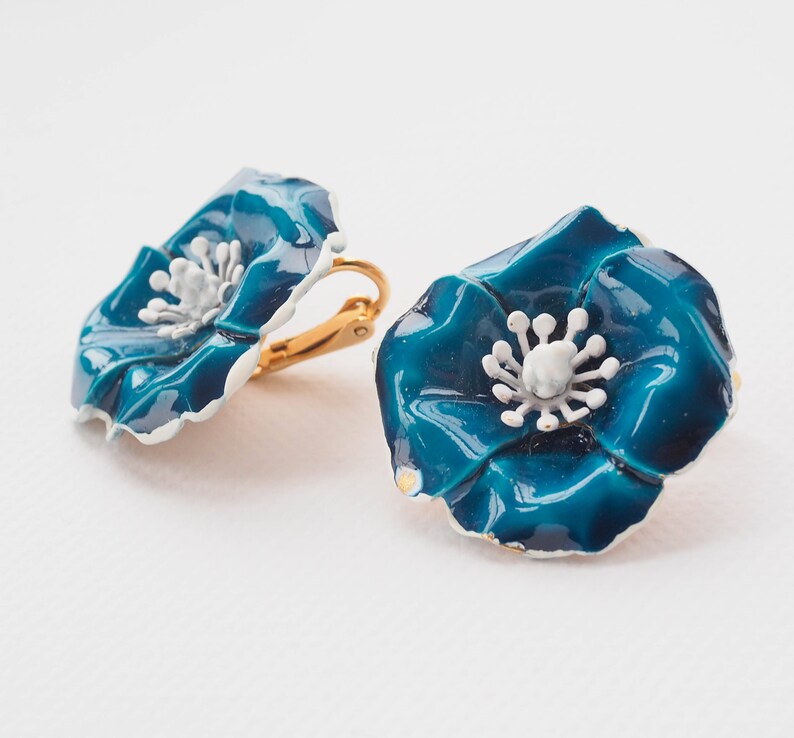 May include: A pair of blue enamel flower clip-on earrings with white centers. The earrings are gold-toned.