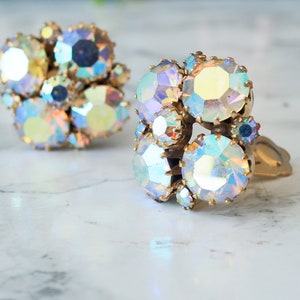 May include: A pair of iridescent clip-on earrings with a cluster of faceted rhinestones set in gold tone metal.
