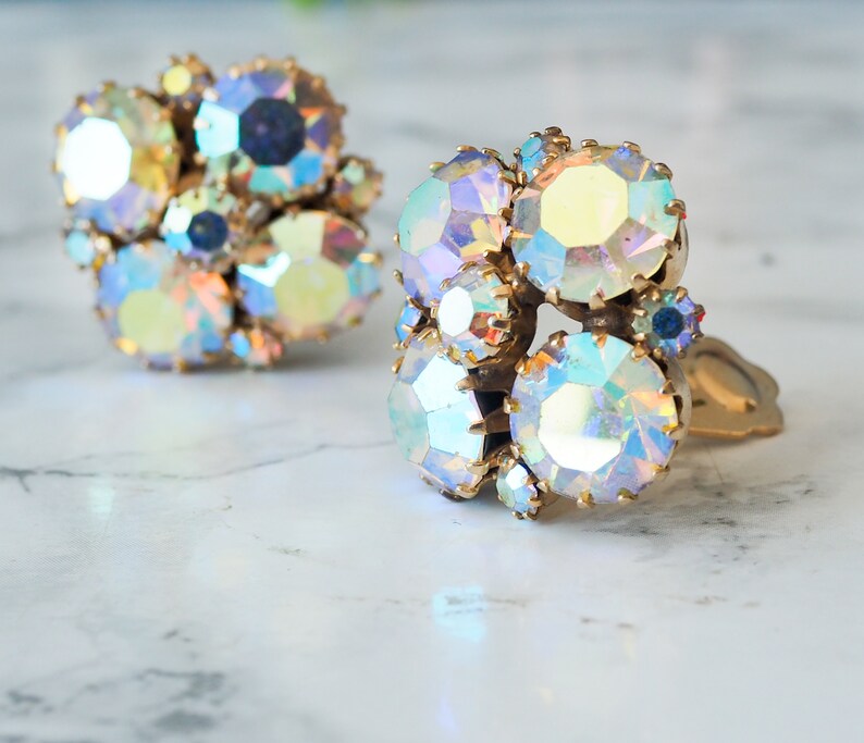 May include: A pair of iridescent clip-on earrings with a cluster of faceted rhinestones set in gold tone metal.