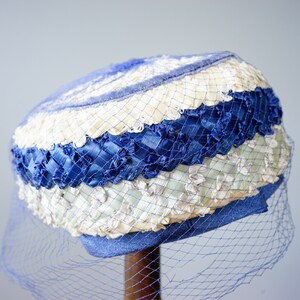 May include: A vintage hat in blue, cream, and white. It has woven ribbon and netting, with a blue veil. A classic accessory.