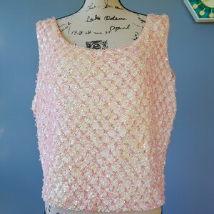 Pu&ograve; includere: Un top senza maniche realizzato con paillettes rosa e bianche. Le paillettes sono disposte a forma di rombo.