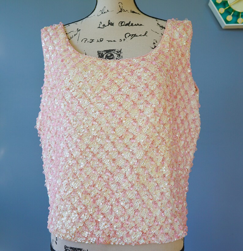 Pu&ograve; includere: Un top senza maniche realizzato con paillettes rosa e bianche. Le paillettes sono disposte a forma di rombo.