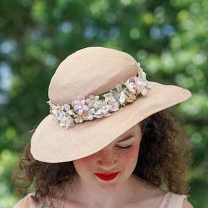 May include: A light brown straw hat with a wide brim and a band of pink, white, and blue fabric flowers.