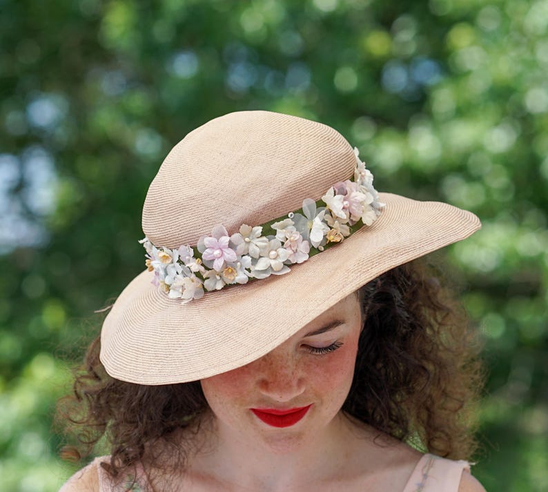 May include: A light brown straw hat with a wide brim and a band of pink, white, and blue fabric flowers.
