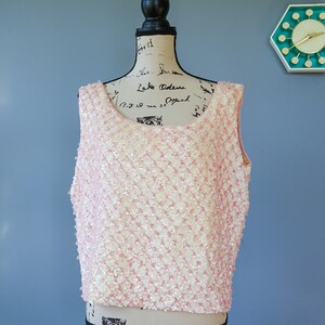 Pu&ograve; includere: Un top senza maniche rosa e bianco con paillettes, con scollo rotondo. Il top &egrave; realizzato in un tessuto strutturato con piccole paillettes rotonde.