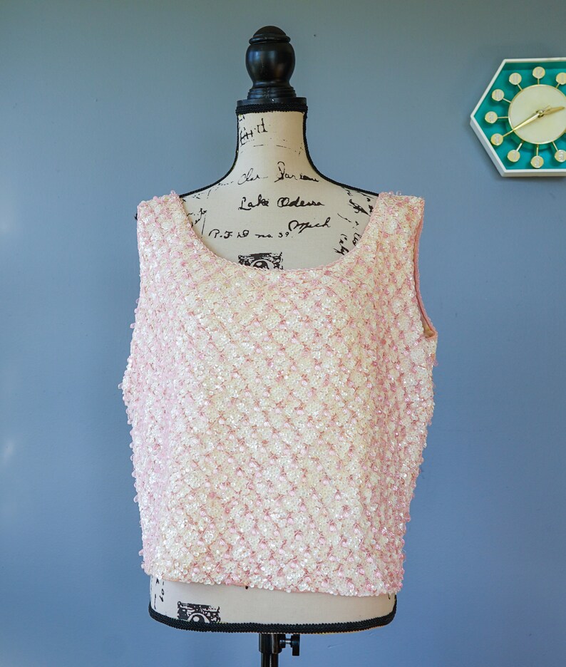 Pu&ograve; includere: Un top senza maniche rosa e bianco con paillettes, con scollo rotondo. Il top &egrave; realizzato in un tessuto strutturato con piccole paillettes rotonde.