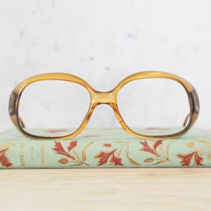 May include: A pair of vintage brown tortoiseshell glasses with large, rounded lenses. The glasses are resting on a small, green book with gold lettering.