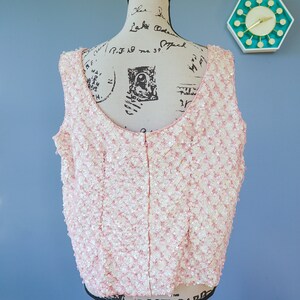 Pu&ograve; includere: Un top rosa senza maniche con una cerniera sul retro. Il top &egrave; ricoperto di paillettes.
