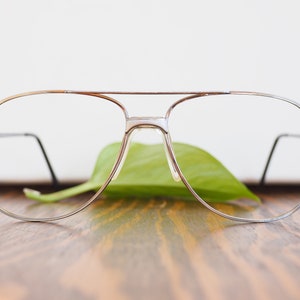 Könnte beinhalten: Silberne Aviator-Brille mit einem grünen Blatt im Hintergrund.