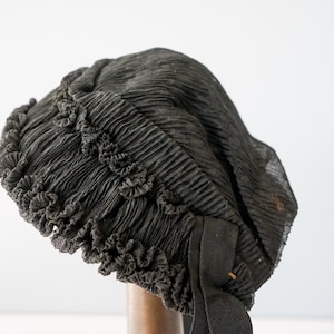 May include: A black, ruffled, fabric hat with a black ribbon. The hat is made of a soft, sheer material and has a delicate, feminine look.