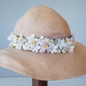 May include: A wide-brimmed straw hat with a band of white and pink flowers.