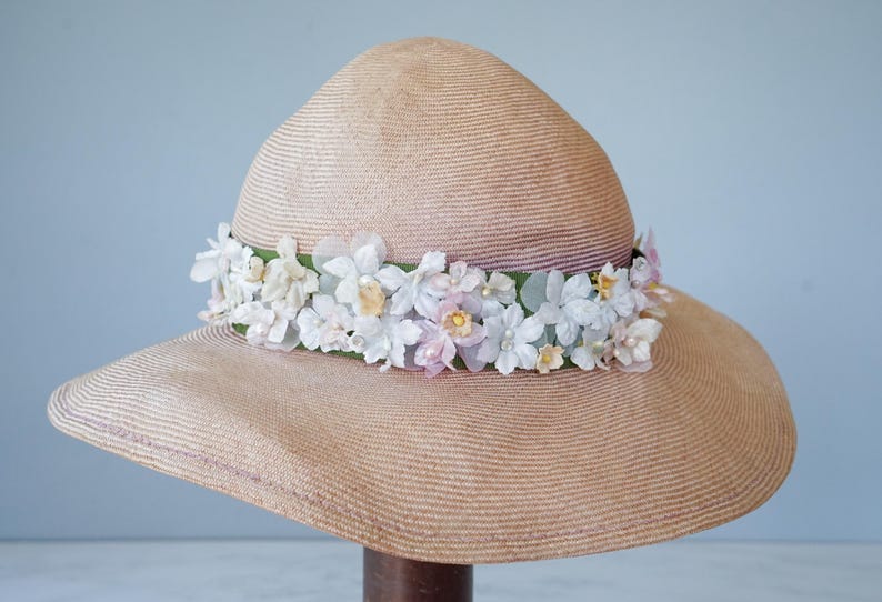 May include: A wide-brimmed straw hat with a band of white and pink flowers.