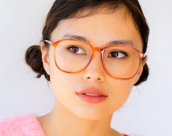 Puede incluir: Una persona joven con cabello castaño que lleva un suéter rosa peludo y gafas con montura marrón. La persona está mirando hacia un lado.