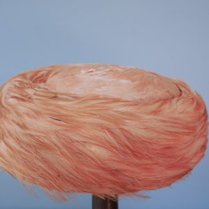 May include: A pink feather hat with a round shape. The hat is made of soft, fluffy feathers and has a smooth, rounded top.
