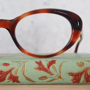 May include: A pair of tortoiseshell oval-shaped spectacles resting on a vintage book with a green cover and gold floral designs.