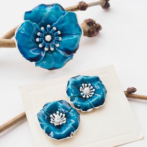 May include: A set of three blue enamel flower brooches with white centers. The larger brooch is a single flower, while the smaller brooches are a pair of matching flowers.