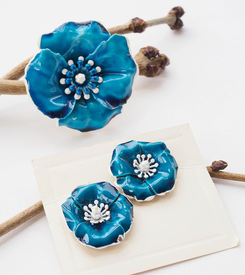May include: A set of three blue enamel flower brooches with white centers. The larger brooch is a single flower, while the smaller brooches are a pair of matching flowers.