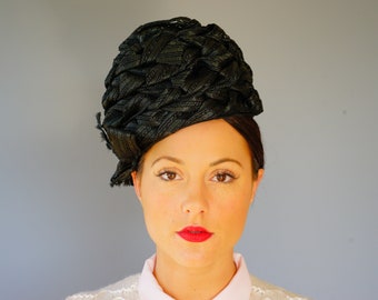 May include: A black, woven hat with a large, rounded crown. The hat is made of a thick, textured material and has a simple, elegant design.