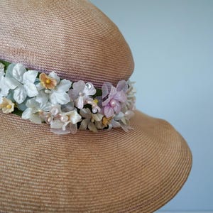 May include: A wide-brimmed straw hat with a band of pink, white, and yellow flowers. The hat is a light brown color and has a woven texture.