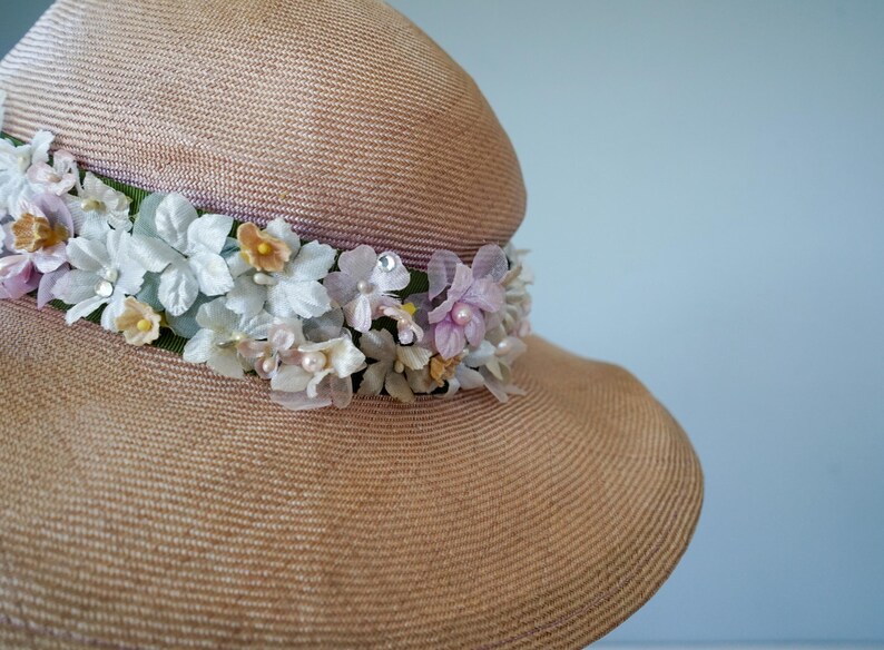 May include: A wide-brimmed straw hat with a band of pink, white, and yellow flowers. The hat is a light brown color and has a woven texture.