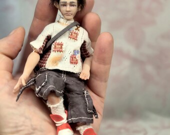 May include: A small articulated doll with dark brown hair, wearing a white short-sleeved shirt with red and blue patch details, dark gray cargo shorts with white stitching, white socks, and red and white sneakers, featuring a dark gray shoulder strap.
