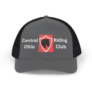 Peut inclure: Une casquette trucker gris anthracite et noir avec un emblème en forme de bouclier rouge et une silhouette de cheval noir au centre. Le texte Central Ohio Riding Club est brodé en blanc sur le panneau avant, de chaque côté du bouclier.