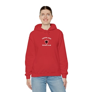 Peut inclure: Un sweat-shirt à capuche rouge vif avec un motif blanc sur la poitrine. Le design comprend un emblème en forme de bouclier avec une silhouette de cheval noire à l'intérieur, entouré du texte CENTRAL OHIO RIDING CLUB en lettres blanches.