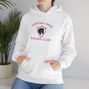 Peut inclure: Un sweat-shirt à capuche blanc arborant un motif de bouclier bordeaux avec une silhouette de cheval noire au centre. Le texte "CENTRAL OHIO RIDING CLUB" est imprimé en lettres bordeaux autour du bouclier. Le sweat possède des manches longues.