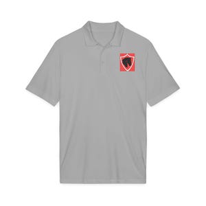 Peut inclure: Un polo gris clair à manches courtes doté d'un col et d'une patte de boutonnage. Sur la poitrine gauche, un écusson rectangulaire affiche un bouclier rouge à bordure blanche, contenant la silhouette noire du profil d'une tête de cheval.