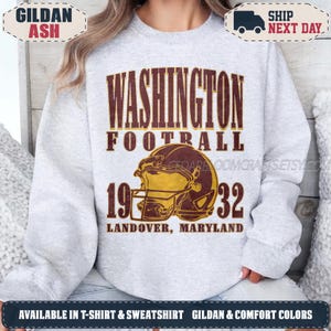 May include: A light gray crewneck sweatshirt featuring a graphic print with the text WASHINGTON FOOTBALL 1932 LANDOVER, MARYLAND. The design includes a yellow and brown football helmet illustration centered between the numbers 19 and 32.