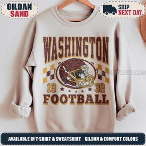 May include: A sand-coloured crewneck sweatshirt featuring a distressed graphic print. The design includes the text WASHINGTON FOOTBALL, the numbers 19 and 32, and a central illustration of a brown football helmet with a yellow face mask.
