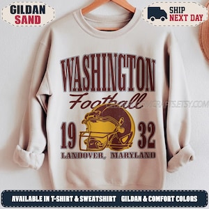 May include: A sand-colored crewneck sweatshirt featuring a maroon and gold graphic. The design includes the text WASHINGTON Football 1932 LANDOVER, MARYLAND and a central illustration of a football helmet in a distressed, vintage-inspired style.