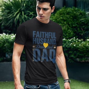 Peut inclure: Un t-shirt noir à manches courtes avec le texte bleu FAITHFUL HUSBAND, une icône de cœur jaune, le mot Devoted et le texte bleu DAD. Le t-shirt est associé à un jean bleu, créant un look décontracté avec un lettrage graphique clair et audacieux.