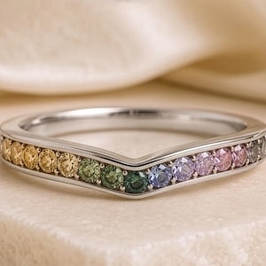 Könnte beinhalten: Ein silberfarbener Ring in Chevron-Form mit einer Kanalfassung, besetzt mit einem Farbverlauf aus runden Edelsteinen in Gelb, Grün, Blau, Violett und Rosa, die in einer durchgehenden Reihe auf der Vorderseite des Rings angeordnet sind.