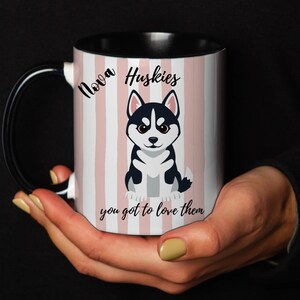 Puede incluir: Una taza de cerámica con asa e interior negros, con un patrón de rayas verticales en rosa claro y blanco. El diseño incluye una ilustración de un husky y el texto en negro Nova Huskies you got to love them en la parte frontal.