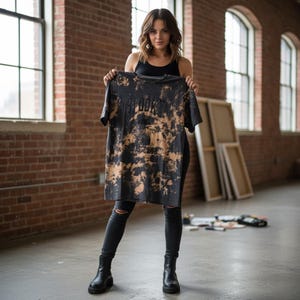 May include: A black short-sleeve t-shirt with a bleached tie-dye pattern featuring the text "SPOOKY" and "BADS CLUB" printed in black on the front. The shirt has a crew neckline and a relaxed fit, showcasing a distressed aesthetic.