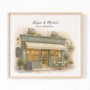 May include: A framed watercolor print of a bakery storefront with a green facade, striped awning, and large display windows. The text reads Alyssa & Michael forever started here, and a small chalkboard sign says FRESH BREAD MADE DAILY.