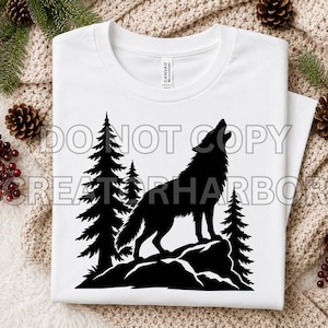 May include: A white short-sleeved t-shirt featuring a black graphic print of a wolf howling on a rock, surrounded by pine trees. The design is centered on the chest area of the garment, which has a crew neckline and a standard fit.