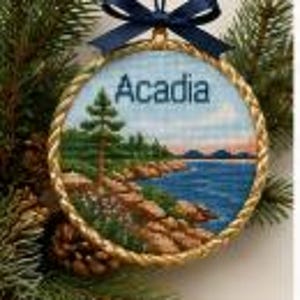 May include: A round hanging ornament featuring a landscape painting of a rocky coastline with a tall evergreen tree and blue water. The word Acadia is printed in dark blue text at the top. The circular frame has a gold twisted rope border.