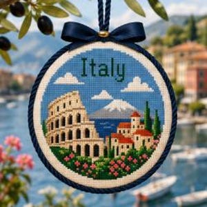 Op de afbeelding: Een cirkelvormig kruissteekborduurwerk met het woord Italy in donkergroene letters. Het ontwerp toont het Colosseum, een kustdorp met rode daken, een blauwe zee en een berg onder een blauwe lucht met witte wolken.